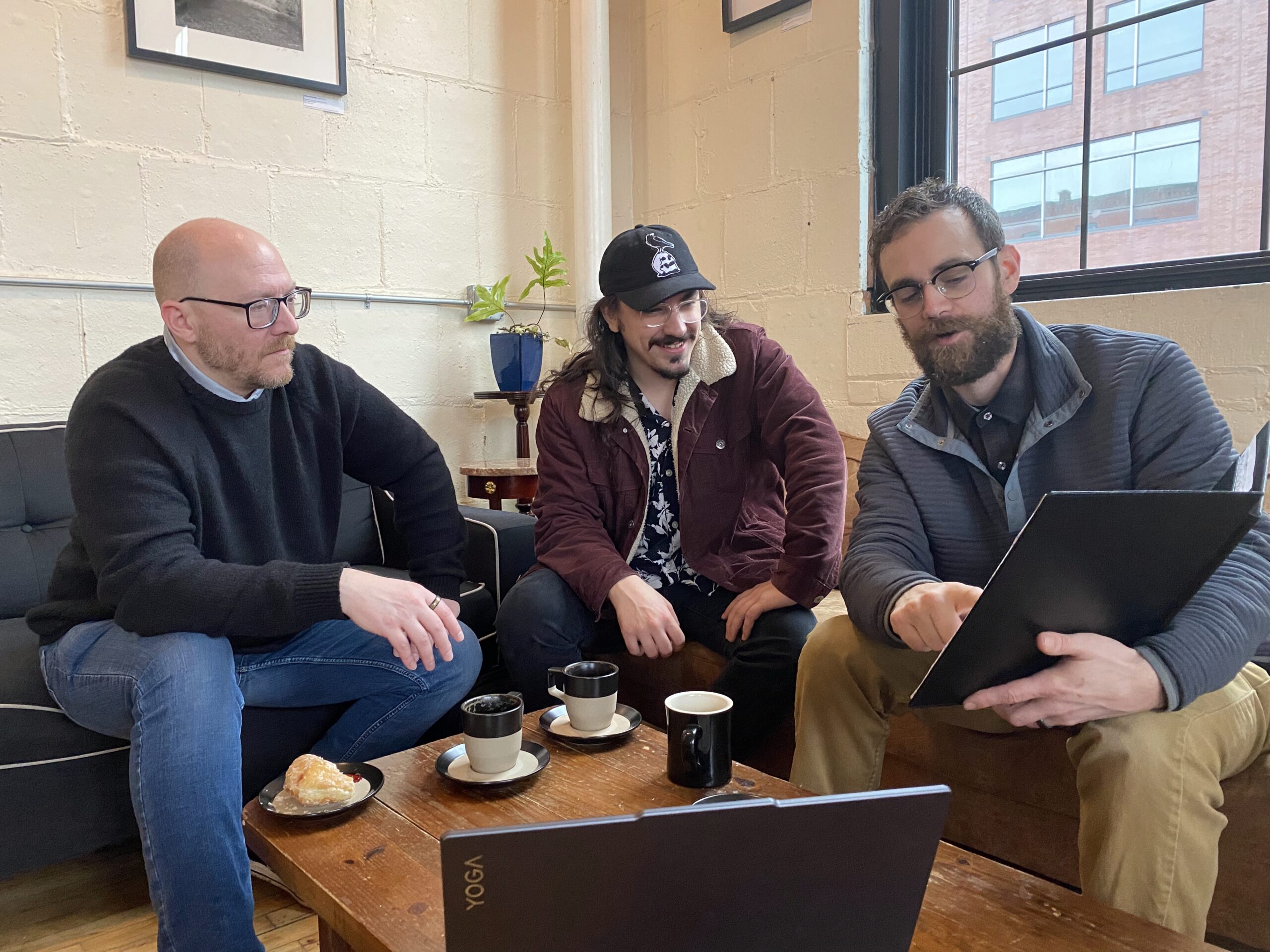 Enablement Marketing founders Rick, Josiah, and Jason sitting together reviewing work on a laptop