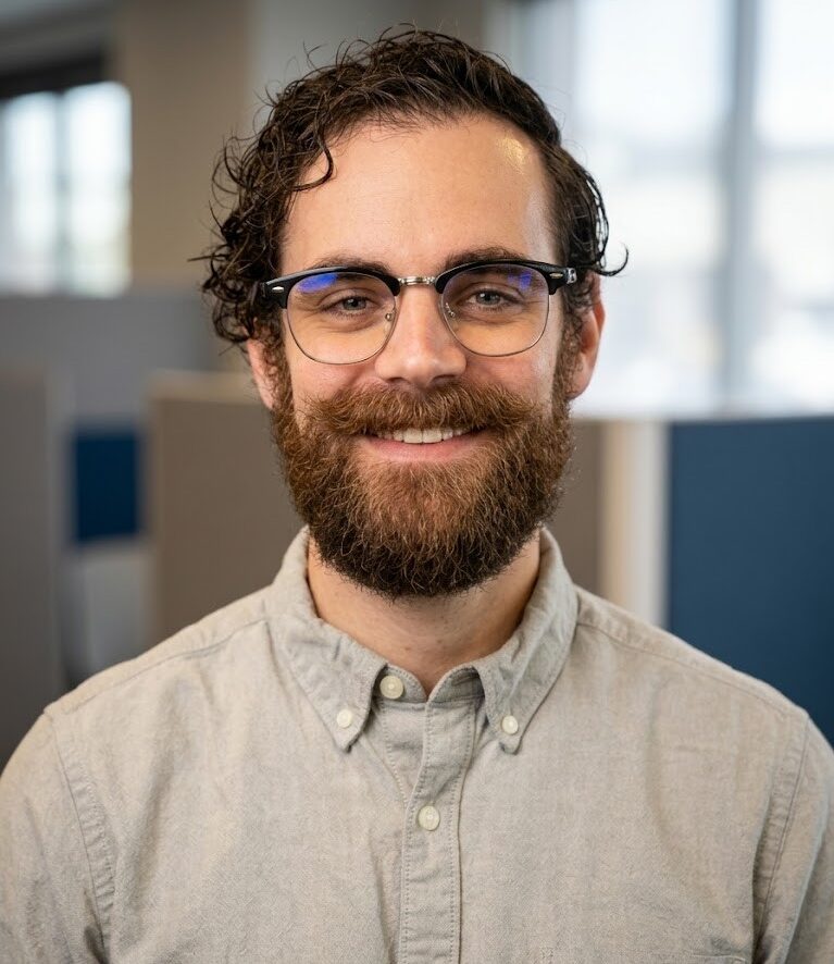 Jason Holmes, Co-Founder of Enablement Marketing, smiling in a professional headshot wearing glasses and a grey collared shirt